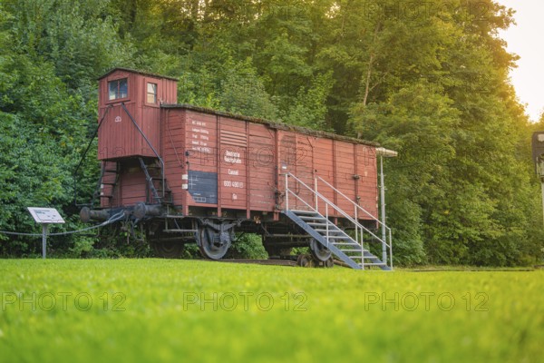 A red goods wagon with steps, green meadow and forest next to it. Nostalgic railway environment,