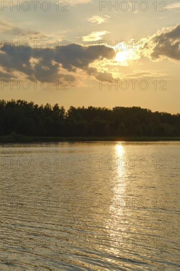A warm summer afternoon unfolds at the lake, with the sun dipping below the horizon. The water
