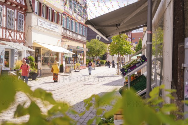 Sunny street in the old town centre with shops and passers-by, surrounded by historic architecture,