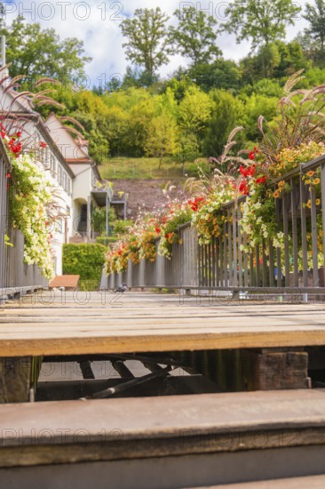 A wooden walkway decorated with flowers leads through a green historical setting, small town of