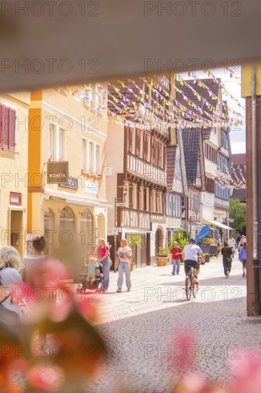 Passers-by and a cyclist in a lively old town street with traditional houses and shops, small town