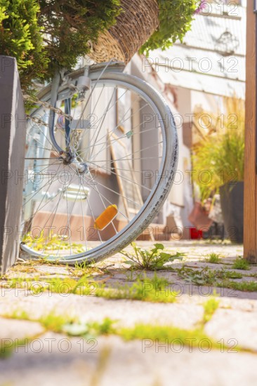 Illuminated bicycle tyre on a flowering basket against an urban background, small town of Perle