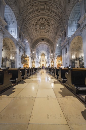 Magnificent church interior with long wooden benches, ornate altar and impressive dome, Munich,