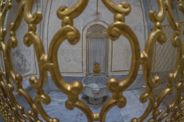 Ornate golden gate protecting a marble fountain inside a historical building in istanbul, turkey,