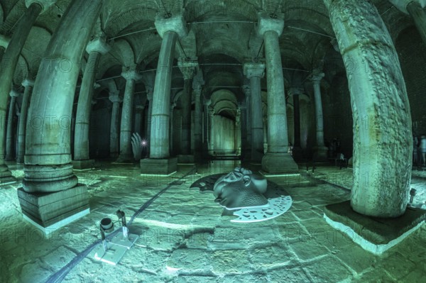 Green lights illuminating ancient columns, medusa's head and hand sculptures in basilica cistern, a