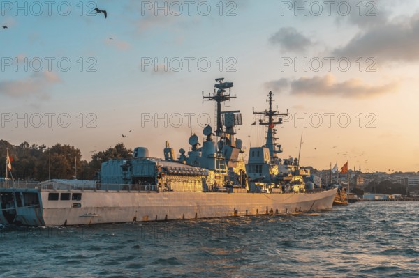 Modern warship gliding through the tranquil sea near istanbul, turkey, under a stunning golden hour