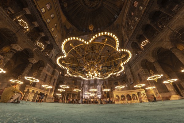 Tourists gather beneath the magnificent chandeliers within the hagia sophia, a historical landmark