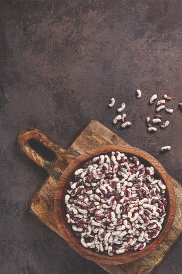 Variegated beans, red with white spots, raw in a wooden bowl, top view, no people