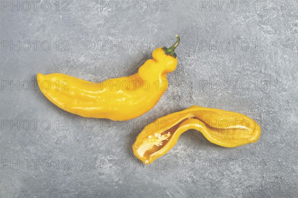 Two unusual yellow peppers are displayed on a textured gray surface. One pepper is whole while the