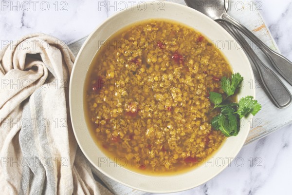 A hearty bowl of lentil soup, rich in flavor and garnished with fresh herbs, is displayed on a