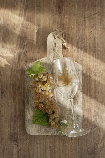 A sprig of white grapes, on a wooden board, with a glass of white wine, top view, natural lighting,