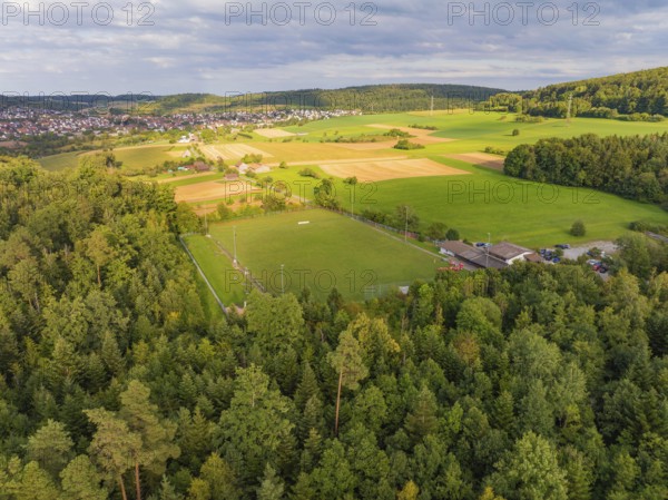 Aerial view of a rural area with a sports field surrounded by forests and fields, close to