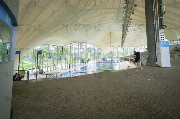 View into an indoor swimming pool with large windows that bring a lot of light onto the pool,