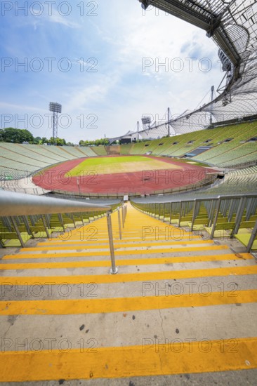 View down the yellow steps to an empty stadium with wide stands and running track, Olympiapark,