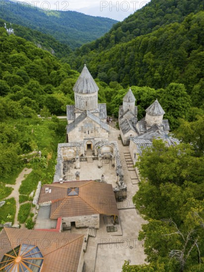 Aerial view of an old monastery complex surrounded by lush green forests, showing historical