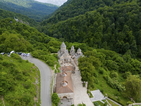 Monastery on a winding road, surrounded by dense natural vegetation and hills, aerial view,
