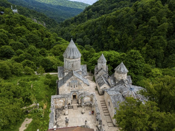 Historic monastery surrounded by dense forest and green hills, impressive stone building, aerial
