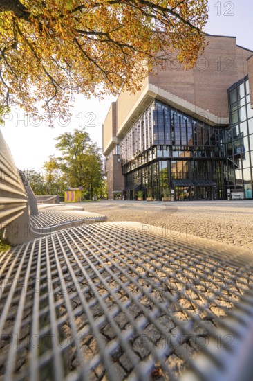 Modern building with glass front, framed by autumnal trees, urban and sunny ambience, Munich,