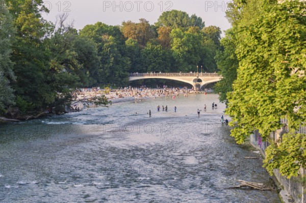 River with people crossing the bridge and relaxing on the bank, surrounded by green nature, Munich,