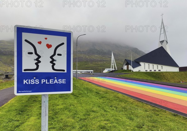 Sign with the invitation to kiss with a street painted in the colours of the rainbow and the