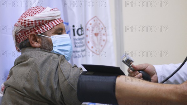 A Syrian doctor wearing a protective mask consults with a displaced patient inside a medical clinic