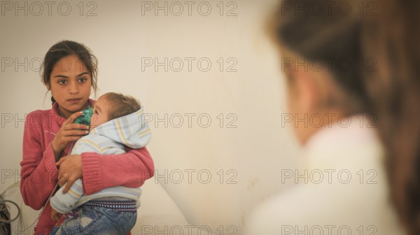 A doctor examining a displaced Syrian child inside a mobile clinic at a refugee camp. Aleppo, Syria