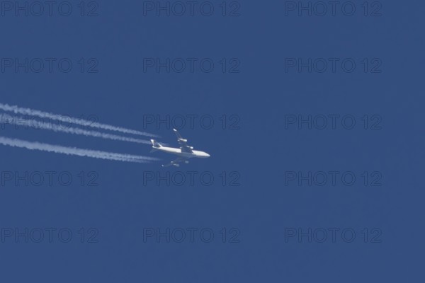 Boeing 747 jumbo jet cargo aircraft with a vapour trail or contrail flying in a blue sky, England,