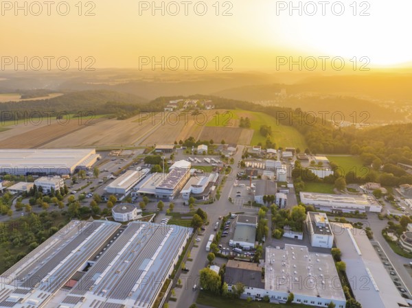 Industrial area in hilly landscape, surrounded by fields, at atmospheric sunset, industrial area