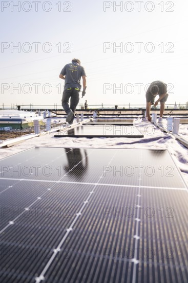 Two workers install solar panels on a sunny roof, PV installation, commercial customers, new build,