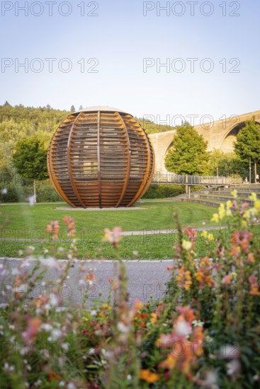 Wooden sculpture in a park with flowers and bridge in the background under a clear sky, Nagold,