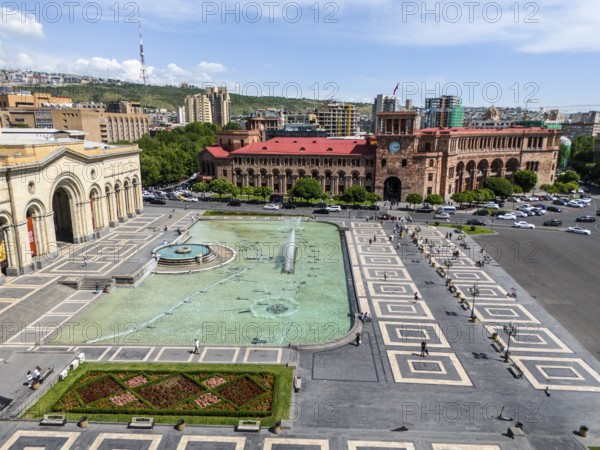 A large square with a fountain surrounded by impressive buildings under a clear sky, aerial view,