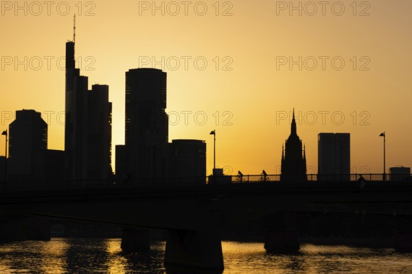 Two cyclists pass the rafter bridge over the Main in the evening while the sun sets behind the