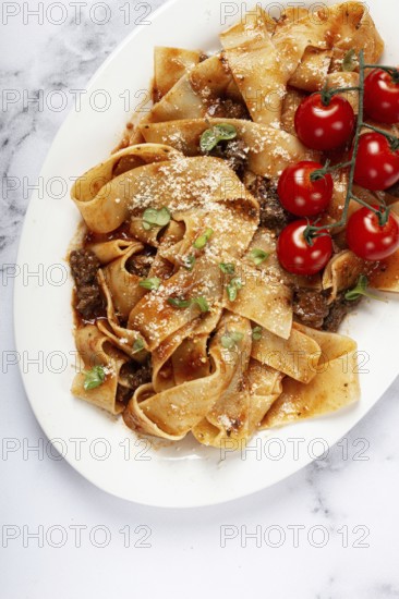 Pappardelle pasta with bolognese sauce, topped with parmesan cheese and cherry branch, homemade, no