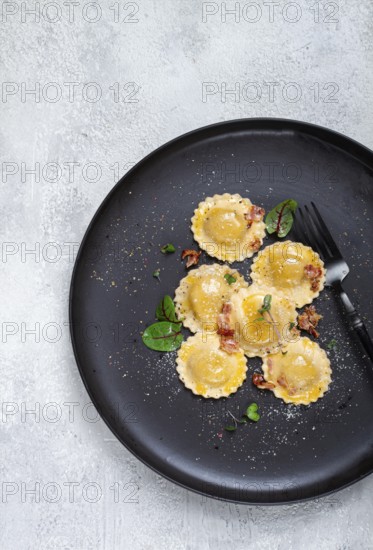 Fresh ravioli, with butter, spices and herbs, fried bacon, on a black plate, top view, dark
