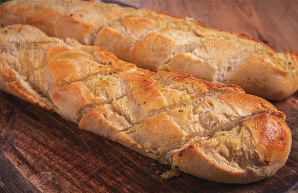 Garlic bread, baguette with garlic butter and herbs, on a wooden board, with herbs and garlic