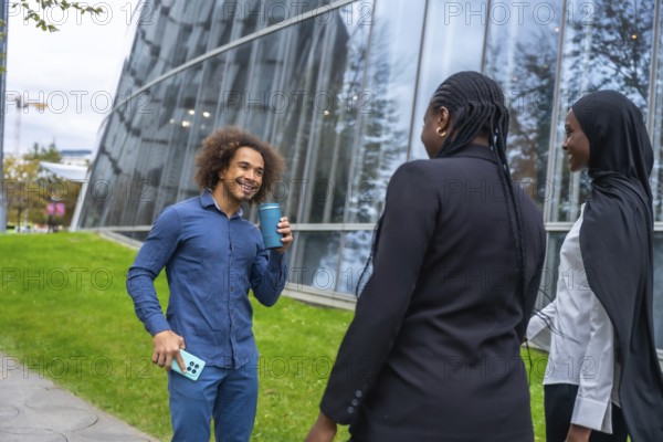 Diverse colleagues are enjoying a casual coffee break outdoors, talking and smiling against a