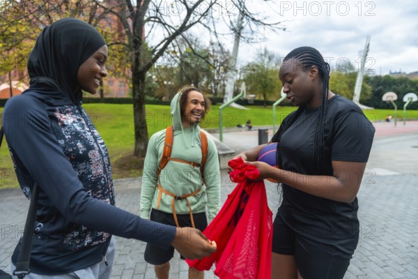 Three diverse friends, including two women wearing sportswear, are cheerfully gathering their gear