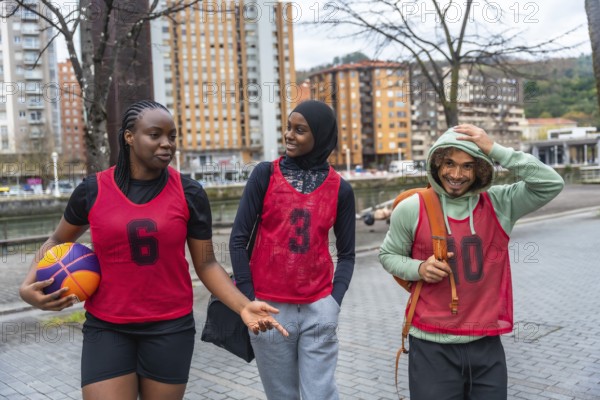 Diverse friends in sportswear and bibs walking and conversing on an urban street, carrying a