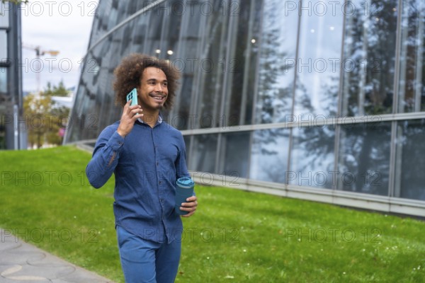 Smiling young Mixed-race man with curly hair walking confidently along a modern office building,