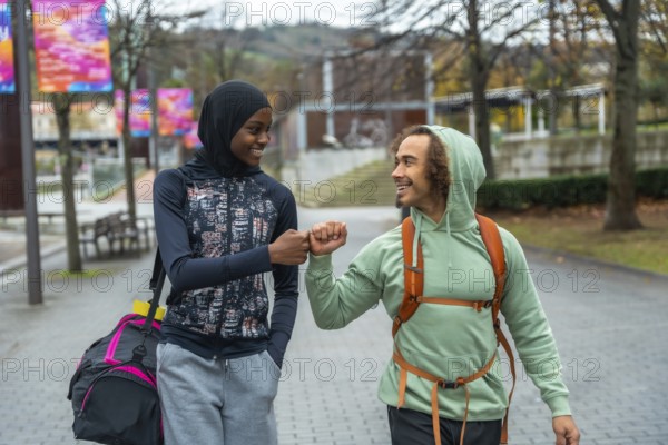 Two young diverse friends in sportswear, one wearing a hijab, smiling and doing a fist bump while