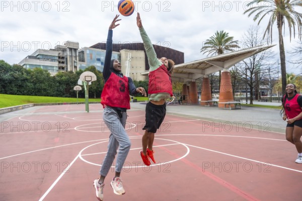 Diverse young women are jumping and reaching for a ball during a friendly outdoor basketball game