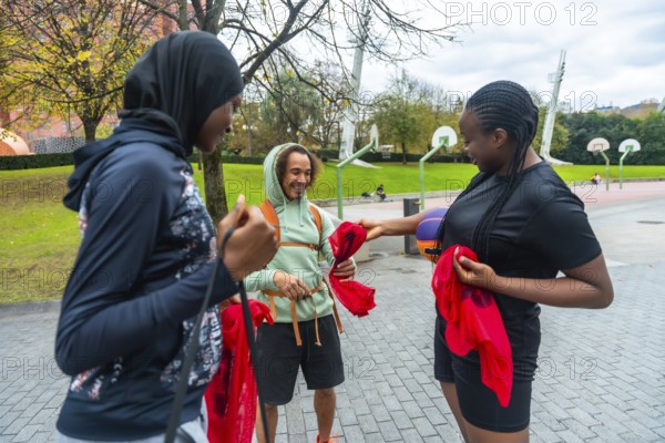 Diverse friends on an urban basketball court smiling and holding red pennants, preparing to play