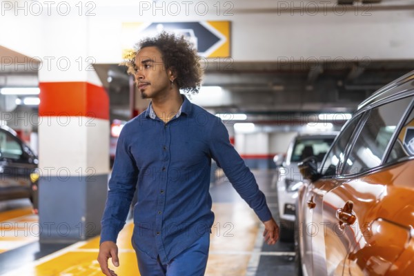 Young man with afro hair walks through a brightly lit underground parking garage, glancing right as