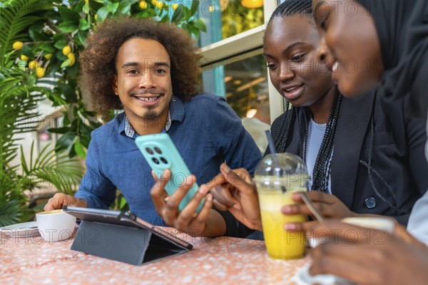 Young diverse friends in a cozy cafe sharing smartphone content, chatting and laughing over coffee