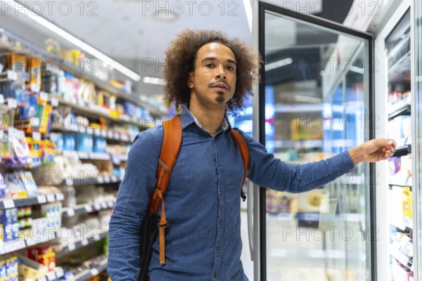 Young man with backpack selecting chilled items from a refrigerated display in a bright modern