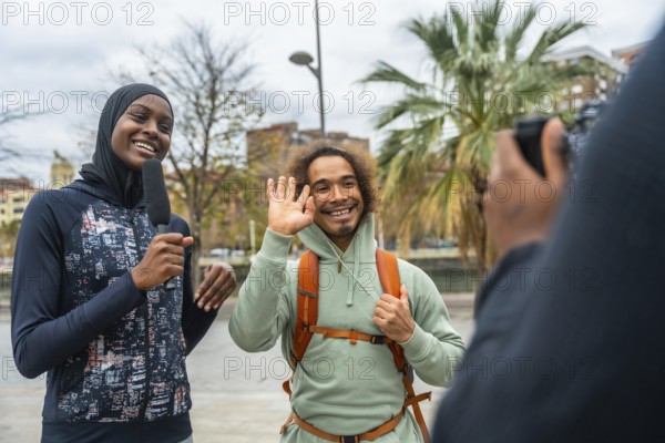 Smiling female journalist wearing a hijab holding a microphone, interviewing a happy man waving on