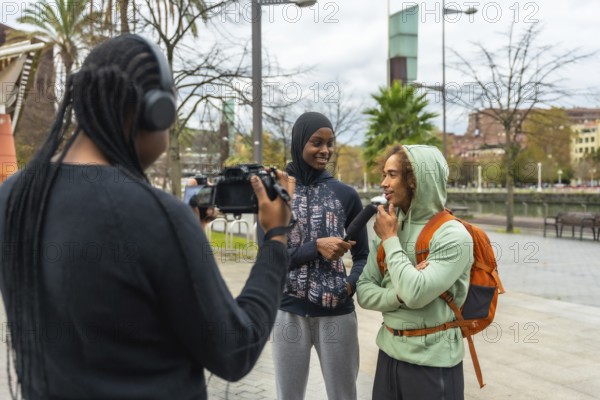 Journalist filming and interviewing a diverse group of young adults in an urban park, capturing
