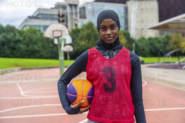 Young muslim woman wearing a hijab, long sleeve shirt, and basketball bib, holding a basketball