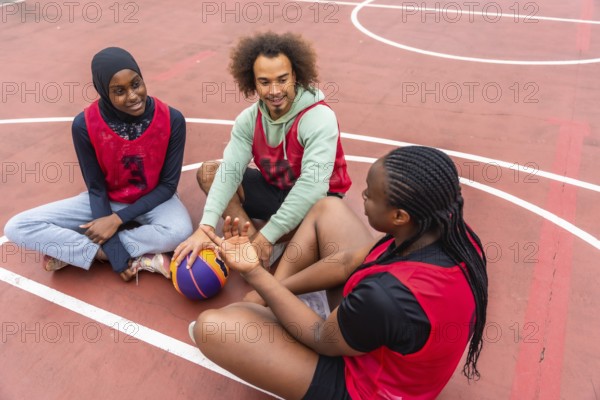 Diverse young friends taking a break on an outdoor basketball court, sitting and talking while