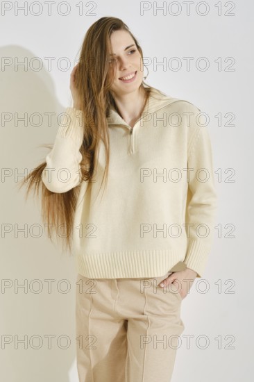 A woman stands in a modern indoor space, smiling with her long hair flowing. She wears a light,